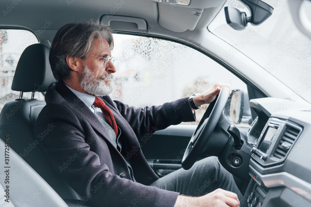 Modern stylish senior man with grey hair and mustache is in the modern car