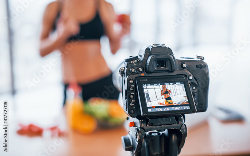 Female vlogger with sportive body standing indoors near table with healthy food