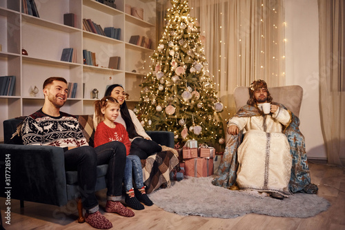Happy family with guy in saint clothes celebrating new year in christmas decorated room