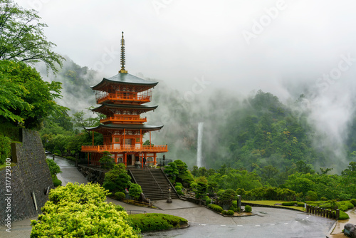 Three-story Sanjudo pagoda of Seiganto-ji temple with Nachi falls and beautiful foggy scenery in the background , listed as a UNESCO World Heritage Site in Wakayama Prefecture , Japan