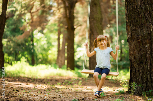 Happy Little girl on a swing in the summer park