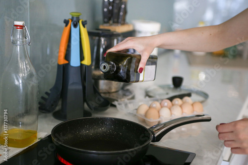 woman cooks fried eggs, pours oil in a pan