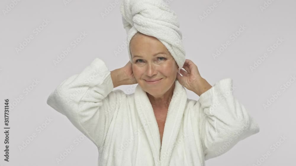 A beautiful adult woman wearing a bathrobe and is touching and correcting a towel over her head isolated over white background A beautiful adult woman wearing a bathrobe and is touching and correcting a towel over her head isolated over white background