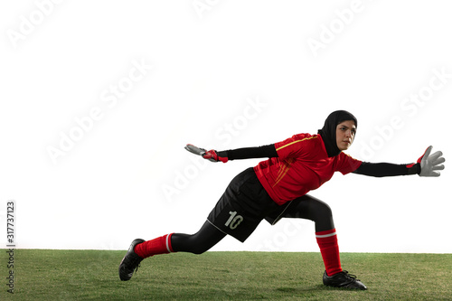 Arabian female soccer or football player, goalkeeper on white studio background. Young woman catching ball, training, protecting goals in motion and action. Concept of sport, hobby, healthy lifestyle.