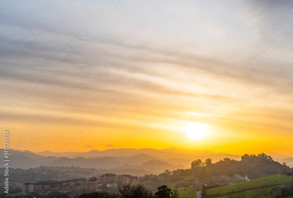 Sunset among the mountain peaks and wooded hills near the city. Cirrus golden and orange clouds. Colorful beautiful landscape