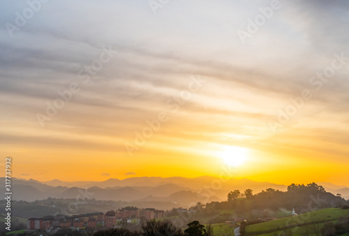 Sunset among the mountain peaks and wooded hills near the city. Cirrus golden and orange clouds. Colorful beautiful landscape