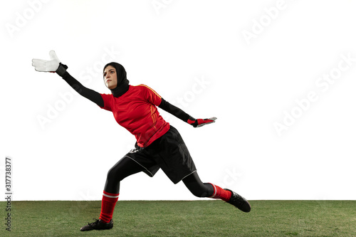 Arabian female soccer or football player, goalkeeper on white studio background. Young woman catching ball, training, protecting goals in motion and action. Concept of sport, hobby, healthy lifestyle.