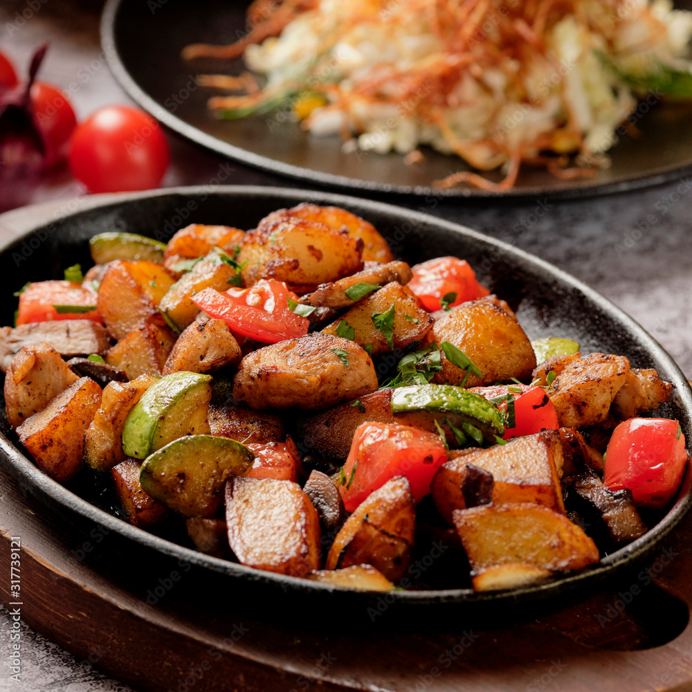 Delicious oven-baked potatoes with herbs and vegetables in a pan, rustic style. Potatoes fried, red cherry tomato, zucchini, onion on gray stone background. Delicious oven-baked potatoes with herbs and vegetables in a pan, rustic style. Potatoes fried, red cherry tomato, zucchini, onion on gray stone background.