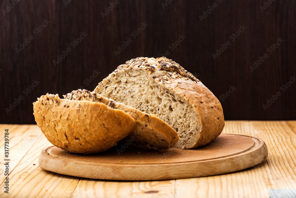 Loaf of wheat bread sprinkled with various seeds, with a cut slices of bread on a wooden table