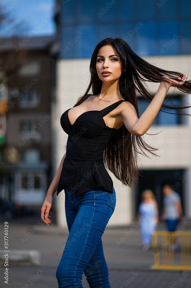 Attractive brunette in a black tank top and jeans on the street. Portrait of a beautiful brunette