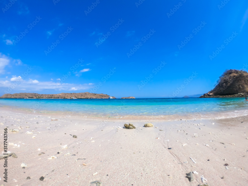 A majestic white sand beach in Komodo National Park, Indonesia, There are some pebbles on the sand. In the back there are other islands. Waves gently washing the shore. Relaxation and chill out