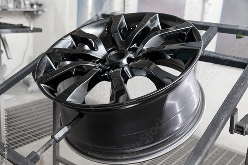 Fotografi A black painted aluminum alloy wheel is mounted on a special frame during drying in a chamber in a vehicle body repair workshop