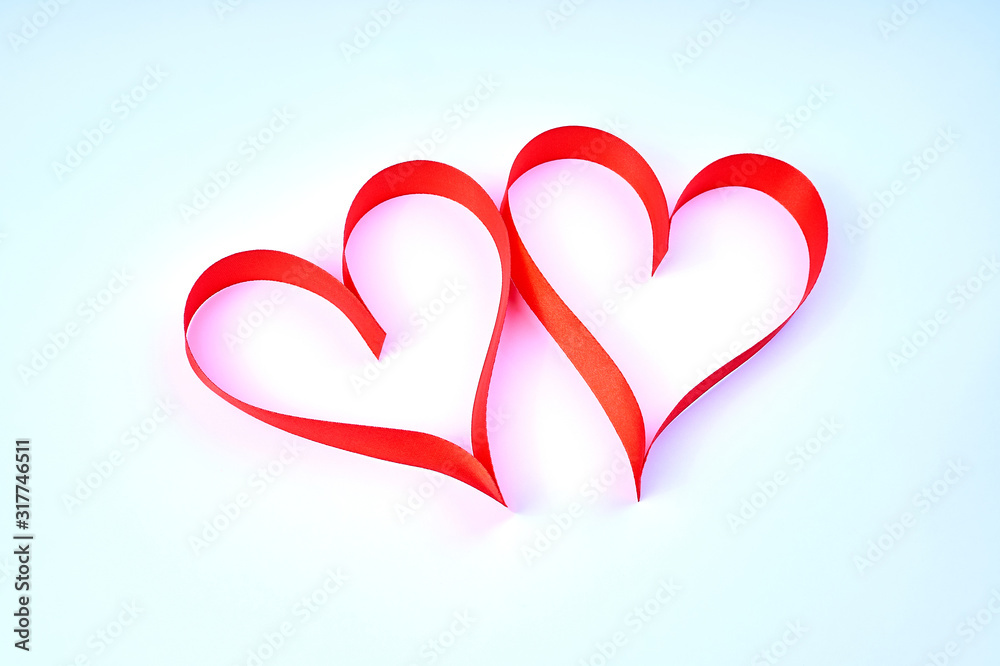 Two hearts with soft shadows made of red satin ribbon lie on a soft blue paper background