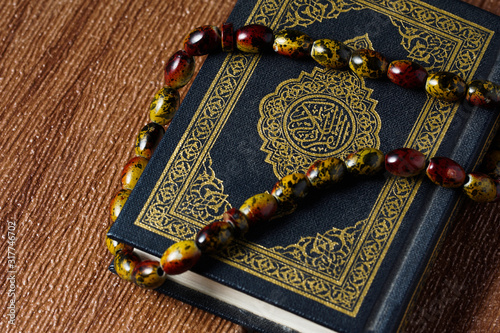 The Quran with rosary beads or “tasbih” and compass on wooden surface. Arabic characters means : Holy Quran, the Holy book of Islam. Islamic concept.