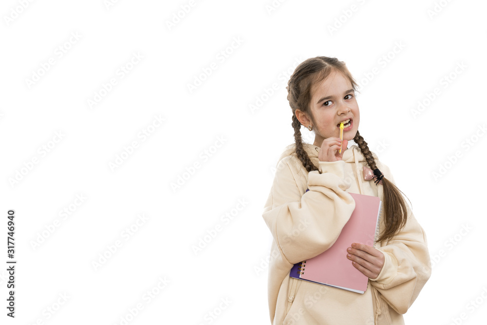 Attractive young girl student with pigtails dressed in beige hoodie holds in hands notebook and pen in mouth, looking at the camera, isolated over white background, copyspace Attractive young girl student with pigtails dressed in beige hoodie holds in hands notebook and pen in mouth, looking at the camera, isolated over white background, copyspace