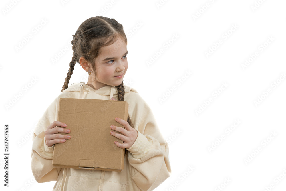 Waist up portrait of the attractive little girl with pigtails dressed in hoodie holds cardboard box in hands and looking at right side, isolated over white background, copyspace Waist up portrait of the attractive little girl with pigtails dressed in hoodie holds cardboard box in hands and looking at right side, isolated over white background, copyspace