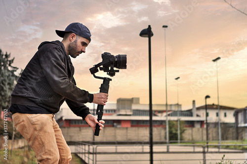 Caucasian videographer filming with cinema gimbal video dslr at sunset , professional video, videographer in event. Cinema lens on gimbal. Medium shot from right side photo