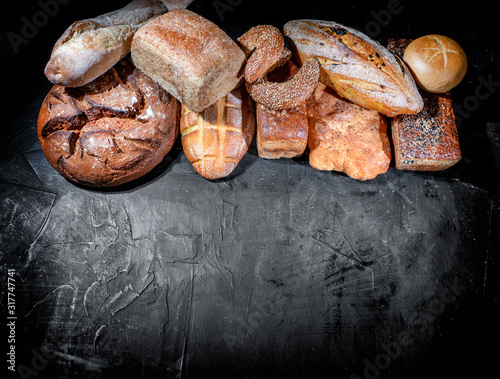 Assortment of fresh baked bread on dark background. White and rye bread, buns with copy place