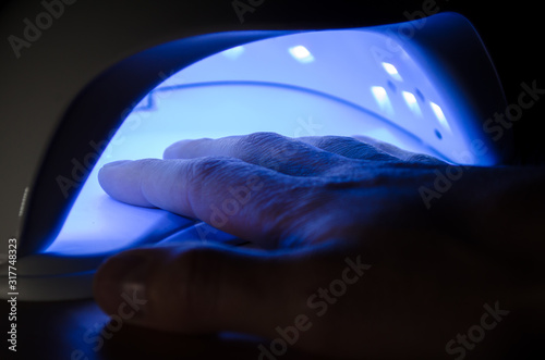 Man hand lies in an ultraviolet lamp with blue shining in a dark room
