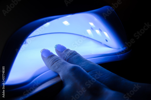 Female two fingers lies in an ultraviolet lamp with blue light in a dark room
