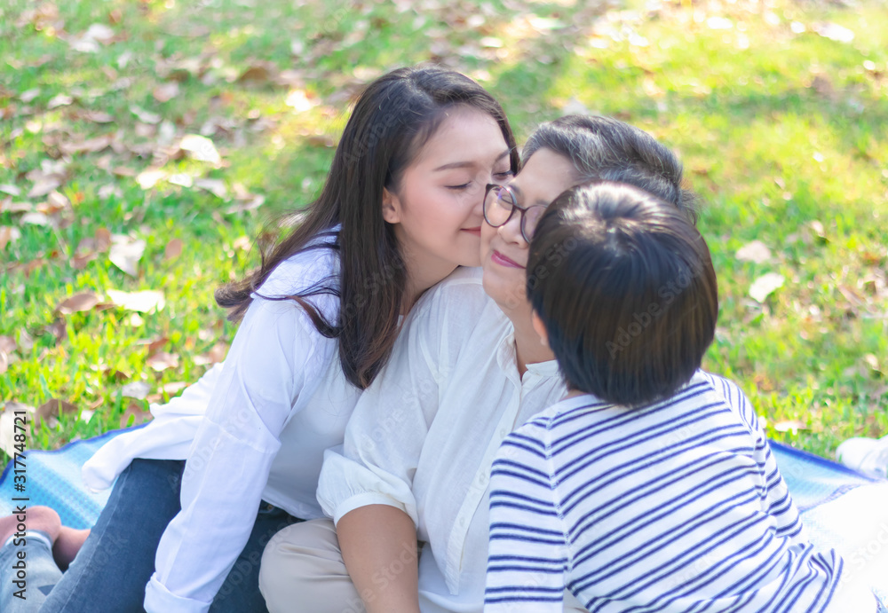 Asian lovely young daughter and grandson kiss happy and healthly senior woman or pleasure grandmother in moment of beautiful love in the park. Family generation relationship or bonding photo concept. Asian lovely young daughter and grandson kiss happy and healthly senior woman or pleasure grandmother in moment of beautiful love in the park. Family generation relationship or bonding photo concept.