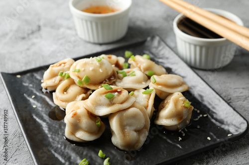 Square plate with dumplings, sauces and chopsticks on grey background, close up