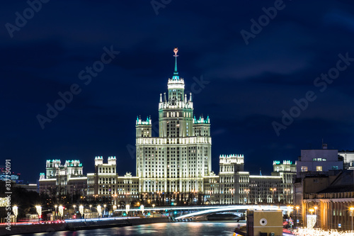 Famous Stalin illuminated skyscraper in Moscow, Russia in the evening blue hour on in the night. View from Bolshoy Moskvoretsky Bridge near Kremlin and Red Square across Moskva river with embankment