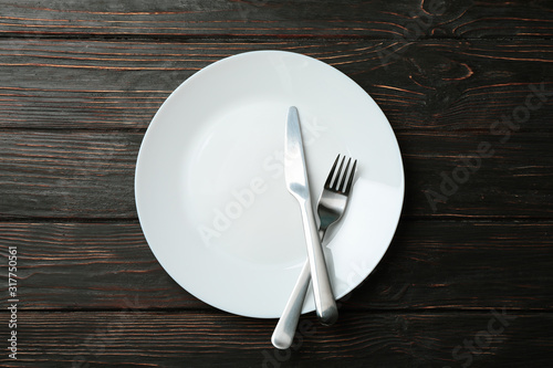 Plate with fork and knife on wooden background, top view