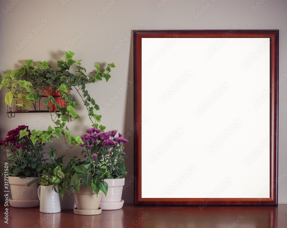 Blank frame  with flower pot decoration on wooden table with white wall background.