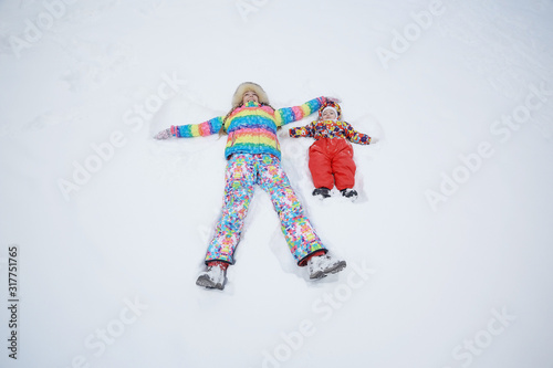 Daughter and mother are playing and lying in the snow in winter outdoors