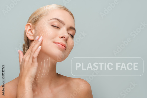 smiling woman touching face with facelift marks isolated on grey with plastic face illustration photo