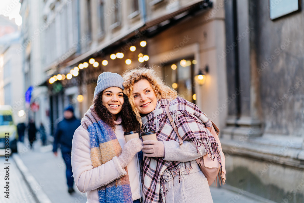 Outdoors fashion portrait of company cheerful pretty girls friends drinking coffee. Walking in the city. Talking and going shopping. Wearing stylish outerwear