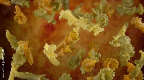 Colored pasta campanelle is flying up on a yellow ochre background in slow motion photo