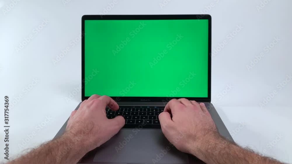 Blank Green screen on a laptop computer. Man pressing buttons on a black keyboard on a silver notebook with green color over the screen. Working on a computer with white backdrop and greenscreen.