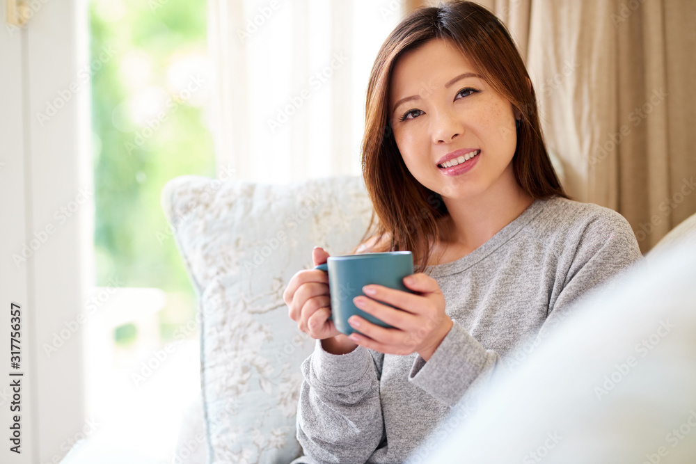 Smiling young Asian woman sitting at home enjoying a coffee Smiling young Asian woman sitting at home enjoying a coffee