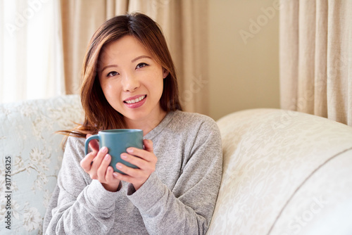 Smiling young Asian woman sitting at home drinking a coffee