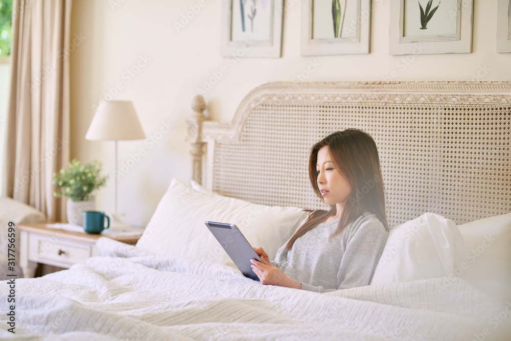 Young Asian woman using a tablet while lying in bed Young Asian woman using a tablet while lying in bed