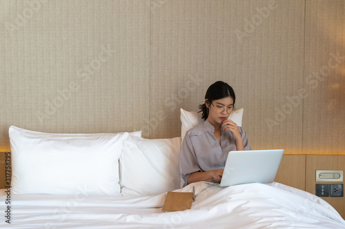 Young asian woman relaxing in the hotel and working with laptop on a bed, Business trip, Working travel concept