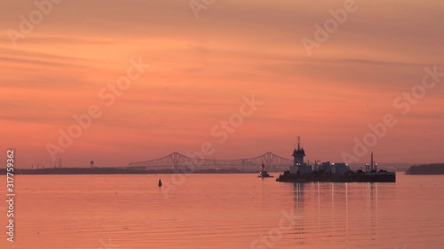 Beautiful Orange And Pink Colors Of The Sunset Glowing By The Sea With Backdrop Of Floating Barge, Moving Tugboat And A Remarkable Commodore Barry Bridge Visible At The Horizon - Wide Shot