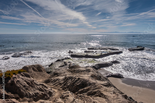 Goleta, CA, USA - January 2, 2020: UCSB, University California Santa Barbara. Worl War II concrete remnants in surf of Pacific Ocean. Dark rocks in front, under blue cloudscape with white stripes. photo