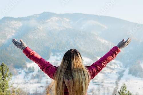 Woman standing with her hands raised facing the mountains in winter time