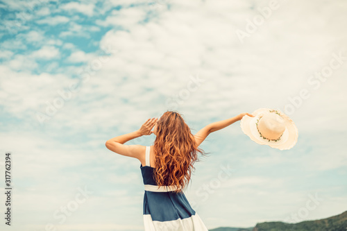 Happy Woman in summer vacation holding hat and wearing dress enjoying the view at the island beach.