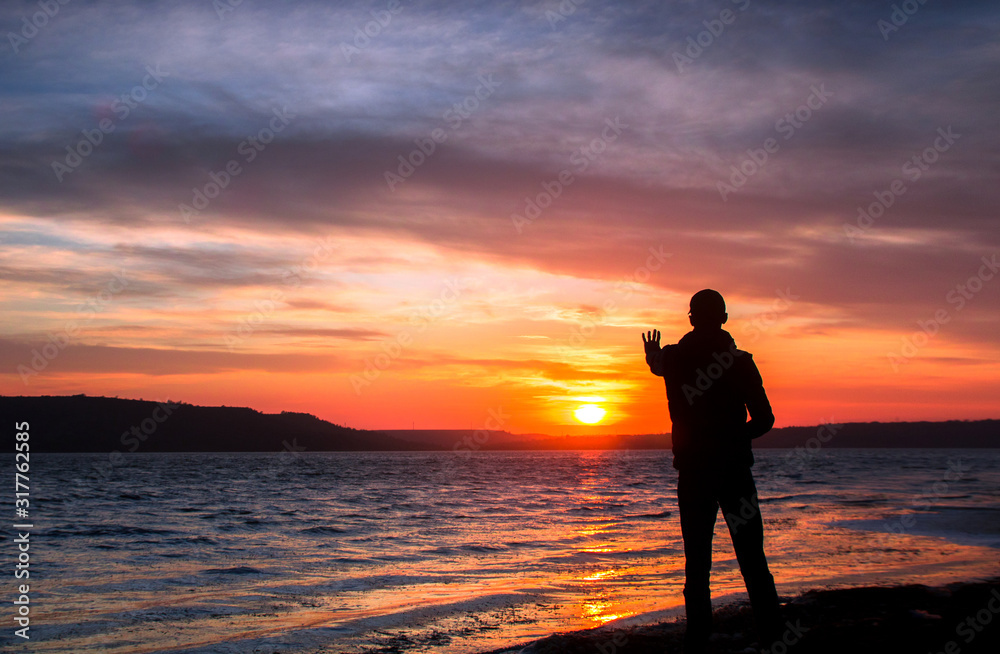 silhouette of a happy unrecognizable man at sunset on the lake