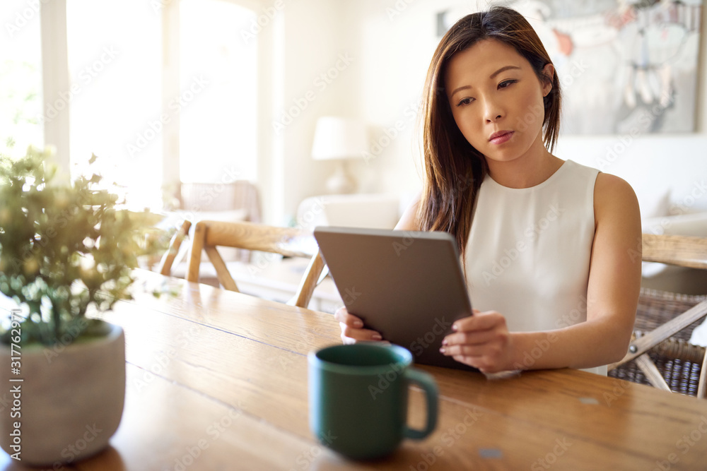 Attractive young Asian woman sitting at home using a tablet Attractive young Asian woman sitting at home using a tablet