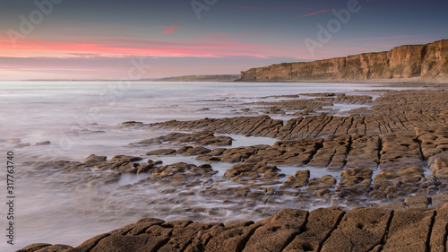 Sea water, washing over a rocky shore, while the sun sets on the horizon. A long exposure has created a milky sea photo