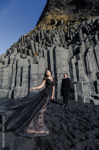 Young beautiful couple bride and groom in black clothes walks near basalt stones in Iceland © Alexander
