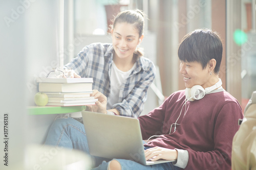Asian young man sitting and using laptop with young woman who bringing the books and helping him in study