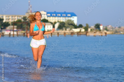 Young woman in sportswear running near still sea edge and smiling © YouraPechkin
