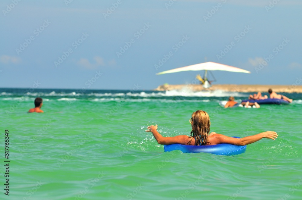 Young woman in bikini backwards in sea water on swimming circle