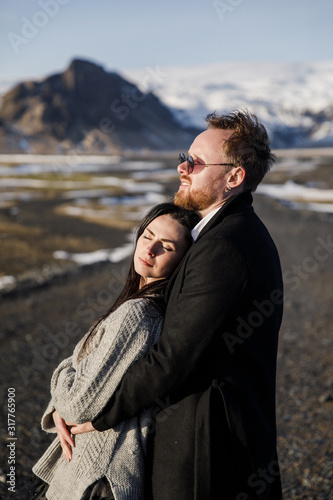 Young beautiful wedding couple in black clothes stands on the road against the backdrop of mountains in Iceland © Alexander